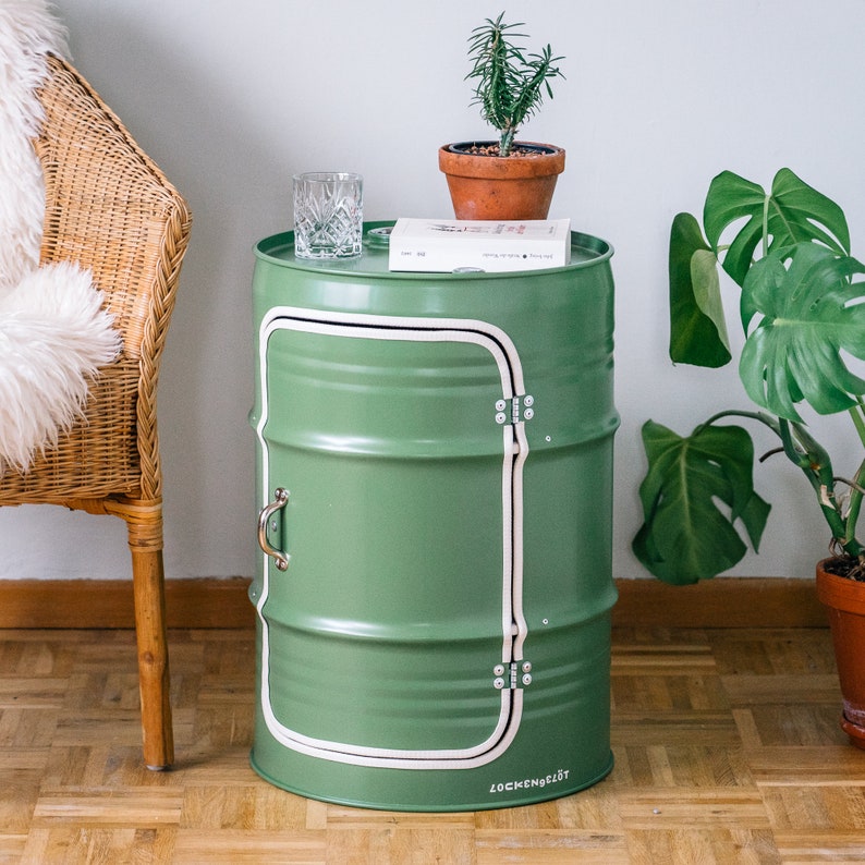 Puede incluir: Un barril de metal verde con una franja blanca y una puerta. El barril se utiliza como mesa auxiliar y tiene un vaso encima. El barril tiene el texto "Lockenberglot" en la parte inferior.