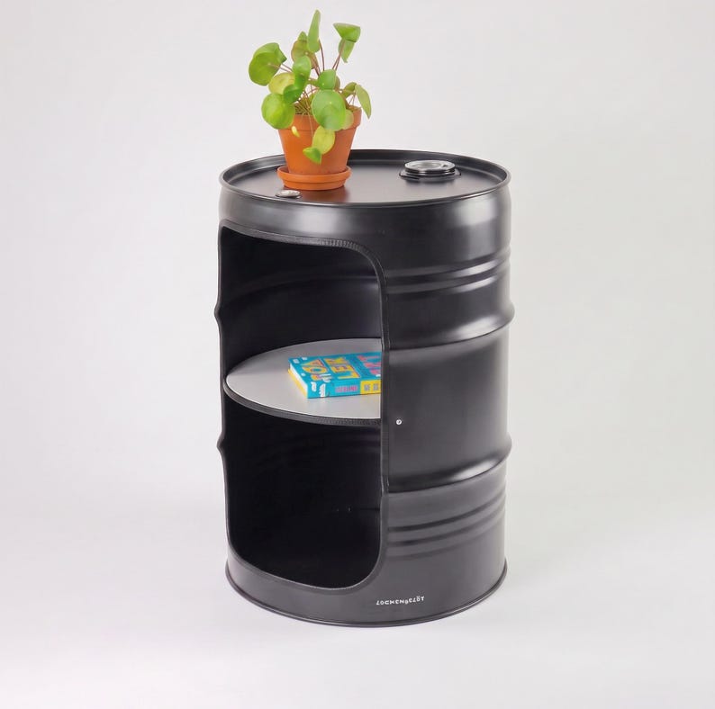 May include: A black metal barrel repurposed as a side table. The table features a cut-out section with a shelf and a potted plant on top. A book rests on the shelf. The table has a industrial aesthetic.