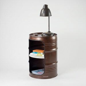 May include: A brown metal barrel repurposed as a side table with a built-in shelf and a small lamp on top. The barrel has a cut-out section for storage, and the lamp has a dark metal shade. Books are visible on the shelf.