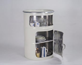 May include: A cylindrical off-white metal cabinet fashioned from a repurposed drum. The unit features two open-front storage levels and a hinged door on the lower section, revealing interior shelves stocked with various ceramic dishes and glassware.