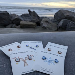 May include: Four cards with different designs of earrings on them. The cards are white with black text and a website address. The earrings are on a white background. The cards are stacked on top of each other. The text on the cards reads "www.bytheirishsea.com".