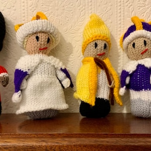Könnte beinhalten: Sechs gestrickte Puppen, die in verschiedenen Kostümen gekleidet sind, darunter ein Polizist, ein königlicher Wächter, eine Königin, ein König, ein Narr und ein Feuerwehrmann. Die Puppen stehen alle auf einer Holzoberfläche.