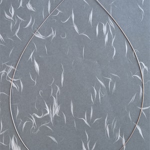 May include: A silver chain necklace with a lobster clasp closure. The chain is lying flat on a gray surface with white fibers scattered across it.
