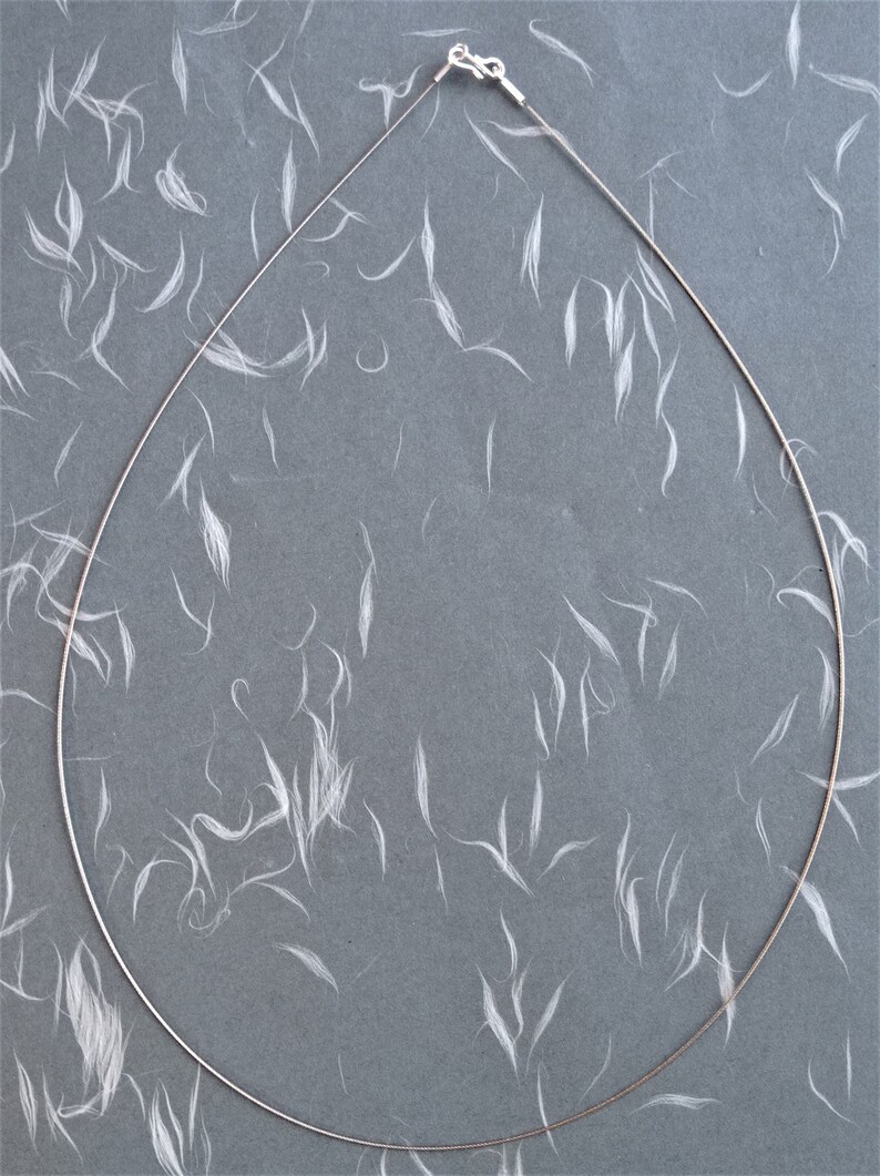 May include: A silver chain necklace with a lobster clasp closure. The chain is lying flat on a gray surface with white fibers scattered across it.