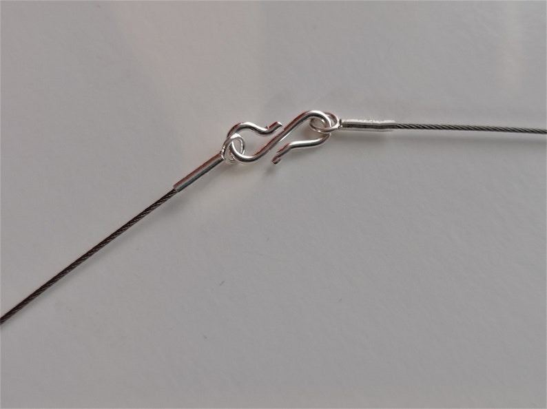 May include: Close-up of a silver clasp on a thin black cable chain necklace.