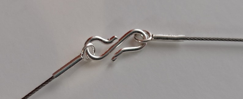 May include: Close-up of a silver clasp on a silver cable chain necklace.