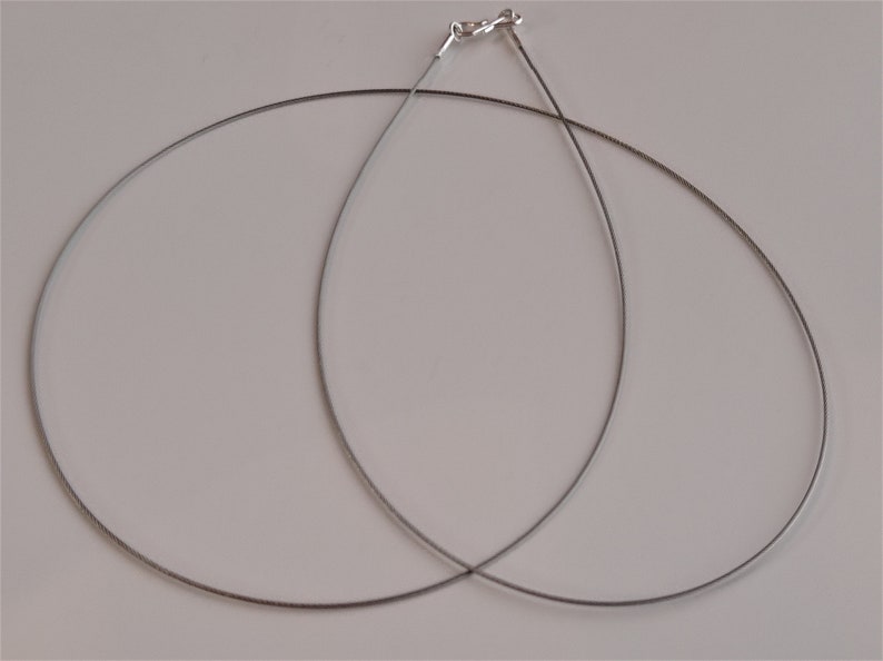 May include: Two silver-toned cable chains, each with a clasp, are lying on a white surface.