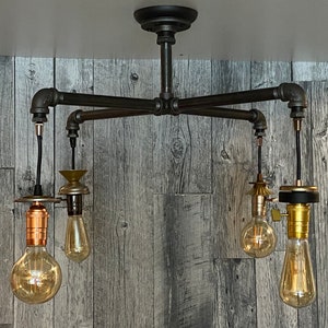 Puede incluir: Lámpara de techo de estilo industrial con cuatro bombillas estilo Edison. La lámpara está hecha de tuberías y accesorios de metal oscuro, con cableado expuesto y portalámparas decorativos. Las bombillas emiten un brillo cálido.