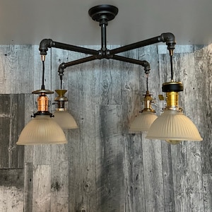Puede incluir: Un plafón de techo de estilo industrial con cuatro luces. El marco de metal negro tiene cuatro brazos que se extienden desde un soporte central. Cada brazo sostiene una luz con una pantalla de vidrio esmerilado y un casquillo de color cobre o latón.
