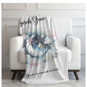 Puede incluir: Una manta de forro polar blanca con un dise&ntilde;o de acuarela de una luna creciente con una cara dormida, estrellas y nubes. El texto "Sarah Grace" est&aacute; escrito en cursiva en la parte superior de la manta. El texto "You are our moon and our stars!" est&aacute; escrito en la parte inferior de la manta.