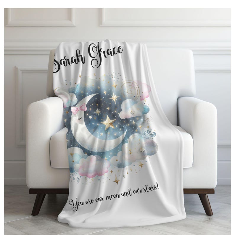 Puede incluir: Una manta de forro polar blanca con un dise&ntilde;o de acuarela de una luna creciente con una cara dormida, estrellas y nubes. El texto "Sarah Grace" est&aacute; escrito en cursiva en la parte superior de la manta. El texto "You are our moon and our stars!" est&aacute; escrito en la parte inferior de la manta.