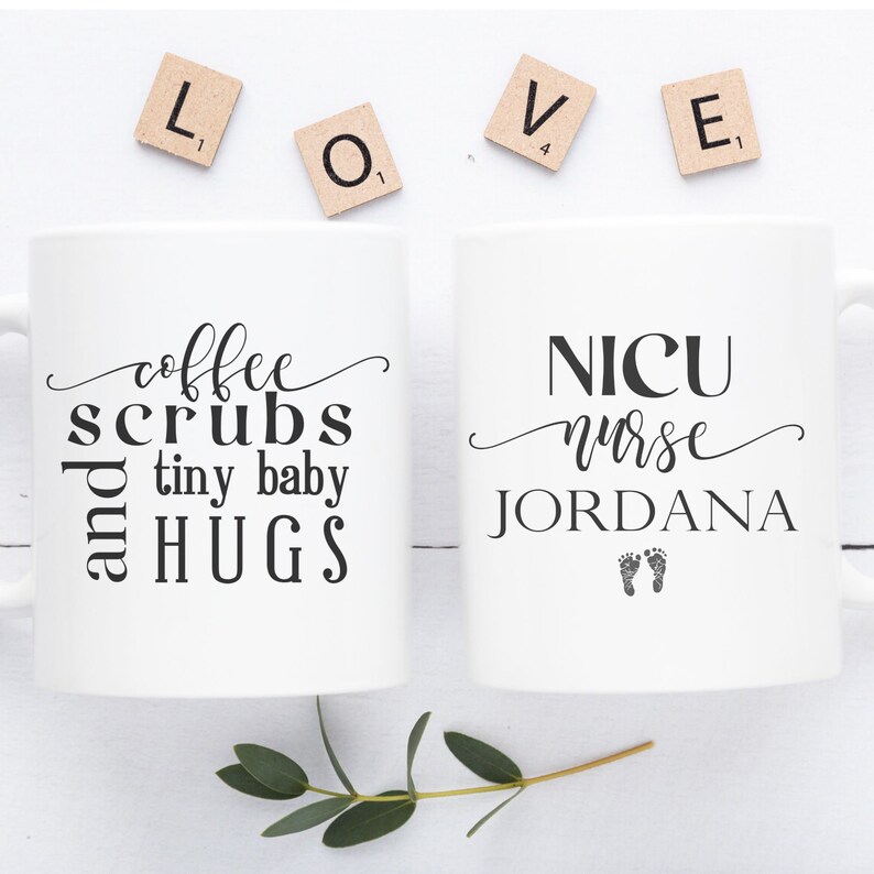 May include: Two white coffee mugs with black text. The mug on the left says "coffee scrubs and tiny baby hugs". The mug on the right says "NICU nurse JORDANA" with two small footprints below the name.
