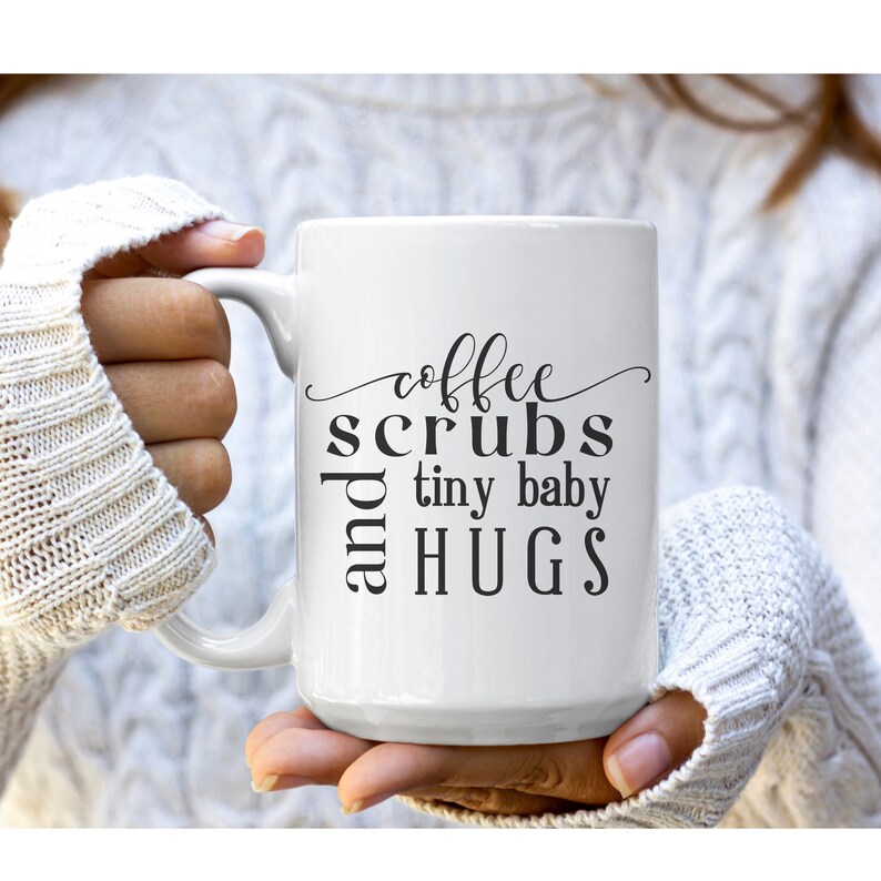 May include: White ceramic coffee mug with black text that reads "coffee scrubs and tiny baby hugs".