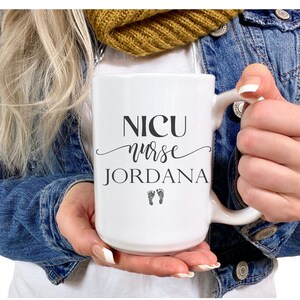 May include: White ceramic mug with black text that reads "NICU nurse Jordana" with two small footprints below the name.
