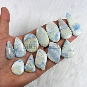May include: A collection of polished gemstones in various shapes, including teardrops, ovals, and irregular forms. The stones feature a swirling pattern of blue, white, and beige hues. The text "NIKHAT GEMS" is visible on the image.