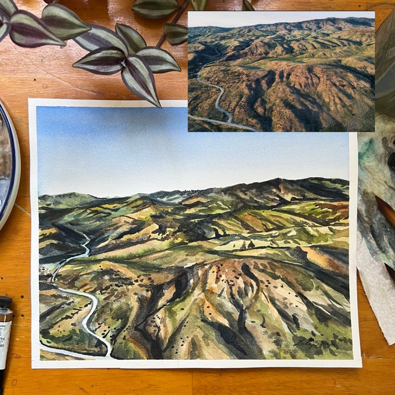 Puede incluir: Pintura acuarela de un paisaje verde, marr&oacute;n y gris con un camino sinuoso. La pintura est&aacute; sobre un fondo blanco.