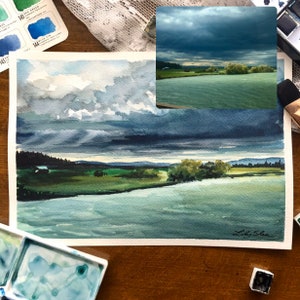 Puede incluir: Pintura acuarela de una escena de r&iacute;o con un cielo nublado. El r&iacute;o es de color azul verdoso claro y el cielo es de color azul oscuro con nubes blancas. La pintura est&aacute; firmada "Laky Shea" en la esquina inferior derecha.