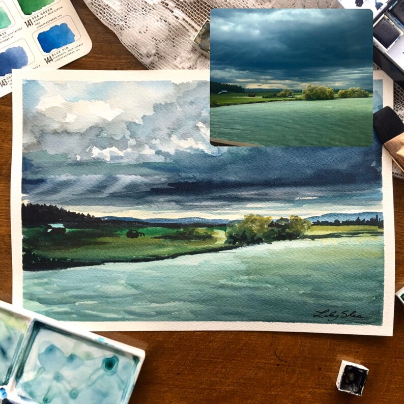 Puede incluir: Pintura acuarela de una escena de r&iacute;o con un cielo nublado. El r&iacute;o es de color azul verdoso claro y el cielo es de color azul oscuro con nubes blancas. La pintura est&aacute; firmada "Laky Shea" en la esquina inferior derecha.