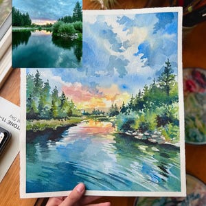 Puede incluir: Pintura acuarela de una escena de r&iacute;o con un cielo de puesta de sol, &aacute;rboles verdes y agua azul. La pintura est&aacute; sobre un fondo blanco.