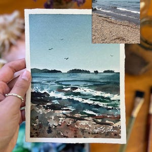 Puede incluir: Pintura acuarela de un paisaje mar&iacute;timo con una costa rocosa, agua azul y algunas aves volando en el cielo. La pintura est&aacute; firmada "Lily Shea" en la esquina inferior derecha.