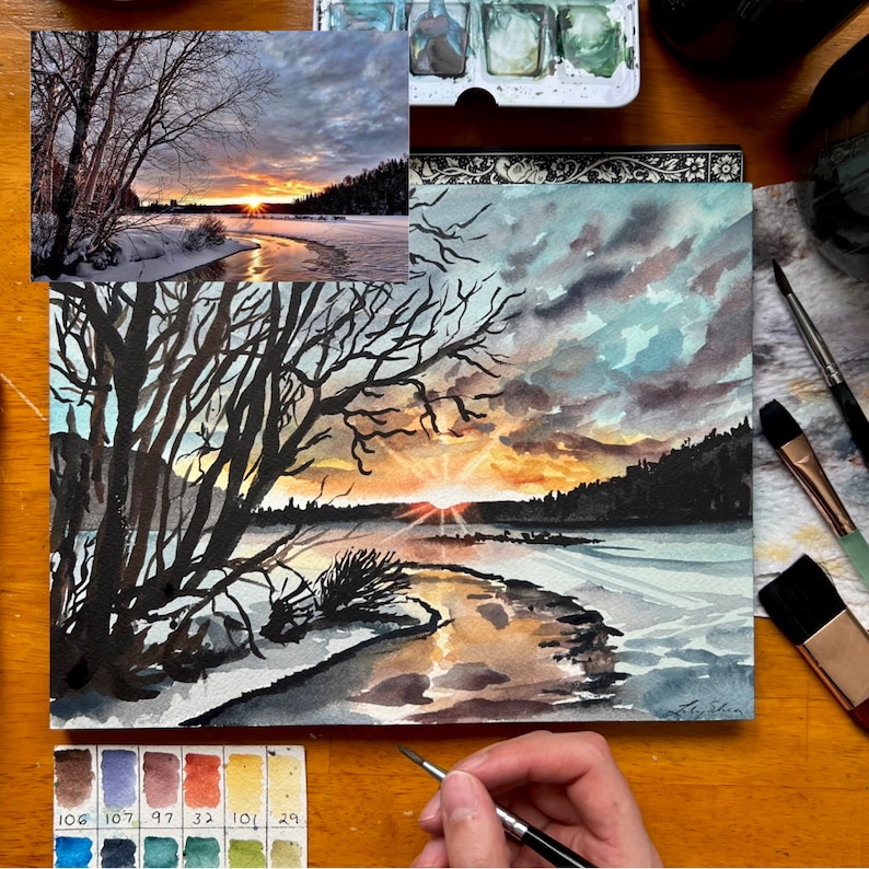 Puede incluir: Una pintura de acuarela de una puesta de sol sobre un lago helado. La pintura presenta una silueta oscura de &aacute;rboles en primer plano y una puesta de sol naranja y amarilla brillante en el fondo. El lago est&aacute; cubierto de hielo y nieve, y el agua refleja los colores de la puesta de sol.