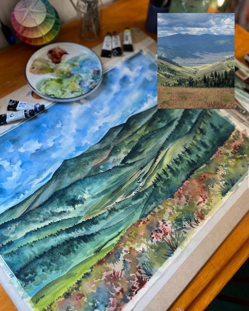 Puede incluir: Una pintura de acuarela de una cordillera con un cielo azul y nubes blancas. Las monta&ntilde;as son verdes y marrones, y hay &aacute;rboles en primer plano. La pintura est&aacute; sobre un lienzo blanco.
