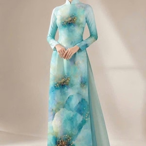 Op de afbeelding: Een vloerlange jurk met een hoge kraag en lange mouwen, voorzien van een aquarel-stijl print in tinten van blauwgroen, blauw en groen met goudkleurige bloemaccenten. Het kledingstuk bevat de tekst XD0303 in de linkerbovenhoek.