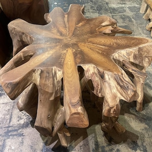 May include: A unique, handcrafted wooden table with a natural, organic design. The table features a starburst-shaped top with a rich, brown color and visible wood grain. The base is formed from the natural roots of the tree, creating a rustic and artistic piece.