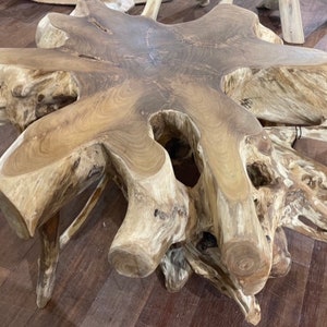 May include: A large, natural wood coffee table with a unique, organic shape. The table is made from a single piece of wood with a natural, rustic finish. The table has a large, flat surface that is perfect for serving food or drinks. The table is also a great conversation starter.