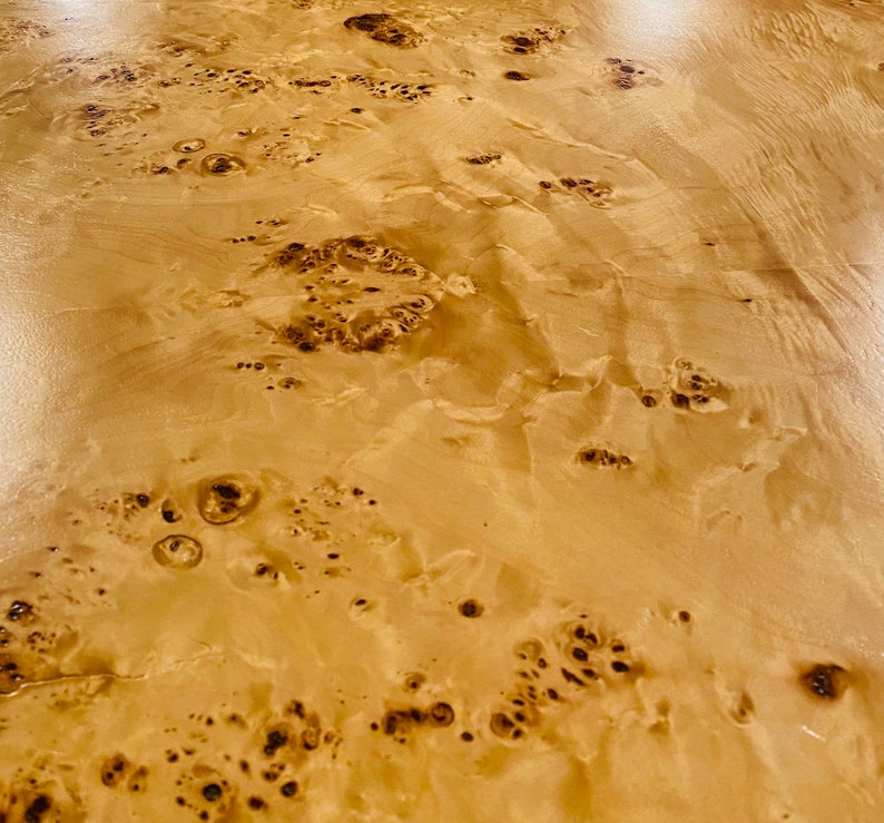 K&ouml;nnte beinhalten: Nahaufnahme einer hellbraunen Holzoberfl&auml;che mit einem einzigartigen Maserungsmuster. Das Holz hat einen nat&uuml;rlichen, warmen Ton und eine glatte Textur.