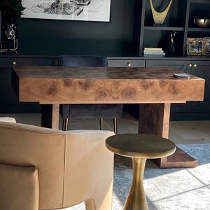 May include: A dark wood desk with a black chair and a gold side table in a home office. The desk has a unique wood grain pattern.