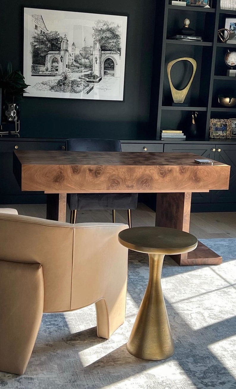 May include: A dark wood desk with a black chair and a gold side table in a home office. The desk has a unique wood grain pattern.