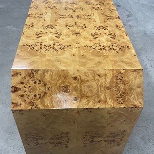 May include: A large, rectangular wooden cabinet with a burl wood veneer. The cabinet has a light brown color with a distinctive pattern of knots and swirls. The cabinet is made of solid wood and has a smooth, polished finish.