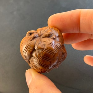 Op de afbeelding: Een klein, ingewikkeld gesneden houten beeldje van een schildpad, met een gedetailleerd schildpatroon en een kleine kikker die erop zit.