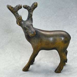 Peut inclure: Une petite figurine en bois de cerf avec des bois. Le cerf est brun et a un visage détaillé. La figurine est debout sur une surface blanche.