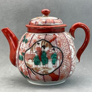 May include: A white porcelain teapot with a red lid and handle. The teapot is decorated with a floral pattern and a scene of four women in traditional Japanese clothing.