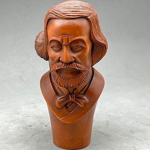 May include: A wooden bust of a man with a beard and a bow tie. The bust is carved in detail and has a warm brown color.