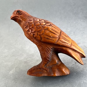 May include: A hand-carved wooden sculpture of a hawk or eagle with detailed feathers. The sculpture is brown and has a natural wood finish.