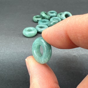 May include: A pile of light green jade donut beads. The beads are smooth and polished, with a slightly translucent appearance.