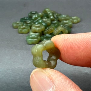 May include: A close-up of a single green gummy candy shaped like a flower. The candy is being held between two fingers. There are many more green gummy candies in the background.