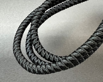 May include: Close-up of a black, braided rope. The rope is tightly woven with a textured surface, and it is looped in a spiral shape. The image is well-lit, highlighting the details of the rope's construction.