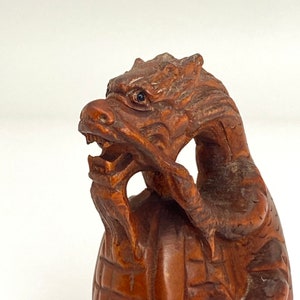 Può includere: Una scultura in legno di un drago con un design dettagliato e intricato. Il drago è avvolto attorno a un oggetto rotondo, probabilmente un guscio di tartaruga.