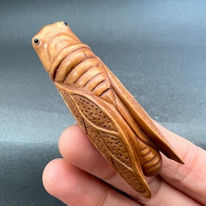 Peut inclure: Une figurine de grillon en bois sculptée à la main avec des détails complexes, y compris un corps texturé et des yeux réalistes.