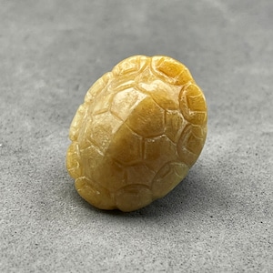 May include: A small, yellow, carved turtle figurine. The turtle is made of a smooth, polished stone and has a detailed shell.