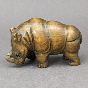 May include: A small, intricately carved wooden rhinoceros figurine. The figurine is brown with a dark brown patina and has a detailed, realistic appearance.