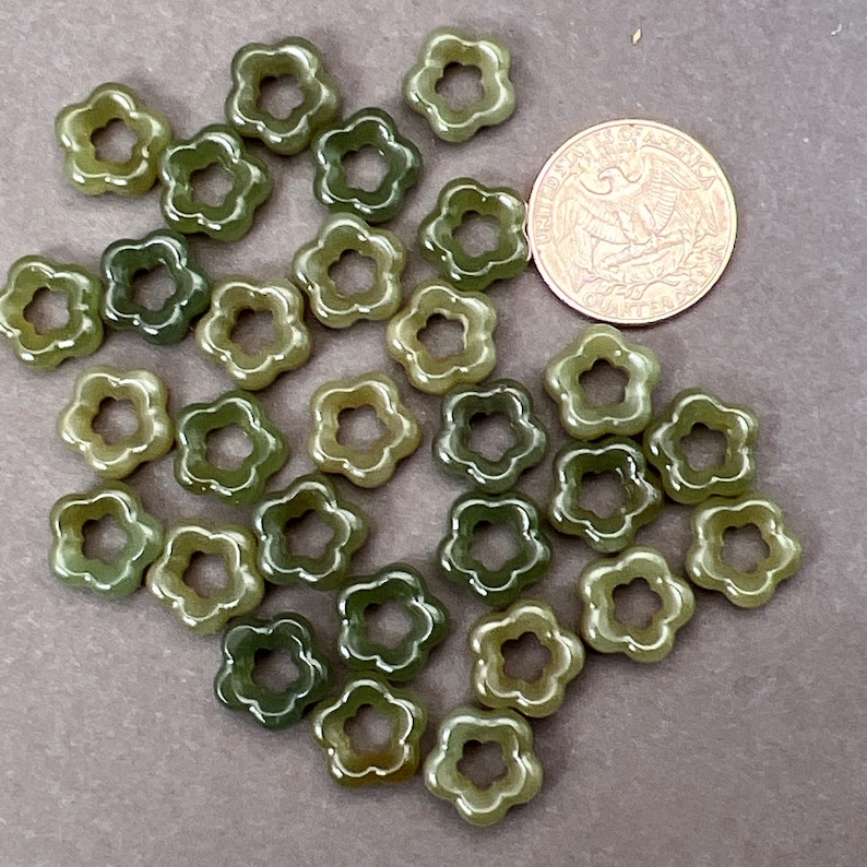 May include: A collection of green flower-shaped beads with a hole in the center. The beads are approximately the size of a US quarter.