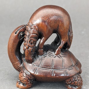 May include: A dark brown wooden sculpture of a horse standing on top of a turtle. The horse is facing the left and the turtle is facing the right. The sculpture is carved in detail and has a smooth finish.