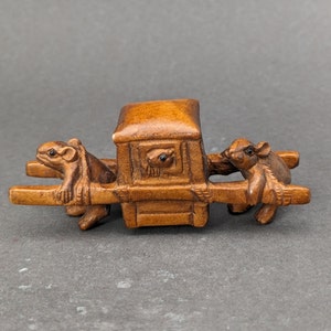 May include: A small wooden sculpture of a palanquin carried by two mice. The palanquin is a traditional Asian sedan chair, and the mice are depicted in a carrying position. The sculpture is made of dark brown wood and has a detailed carving style.