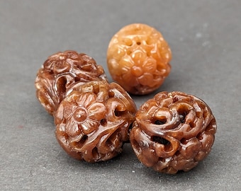 May include: Four intricately carved brown and orange gemstone beads with floral designs. The beads are round and have a smooth, polished finish.