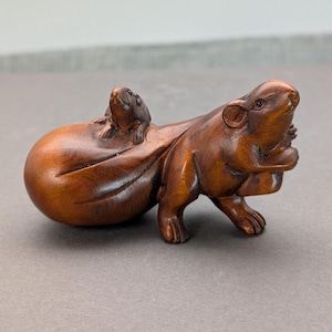 Puede incluir: Escultura de madera detallada de una criatura parecida a un roedor con un roedor más pequeño en su espalda. La escultura es de color marrón intenso, con vetas de madera visibles y detalles intrincados. El roedor más grande parece estar sosteniendo algo.